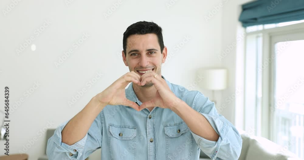 Cheery Hispanic man standing in living room showing hand gestures to camera, demonstrate popular