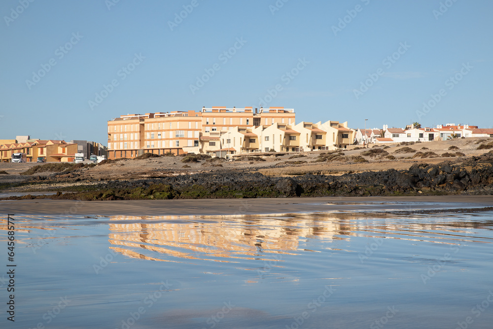Residential neighborhood, near Playa de la Jaquita, reflecting in the waters of the shallow shoreline of the tranquil volcanic sand beach, at El Medano, Tenerife, Canary Islands, Spain