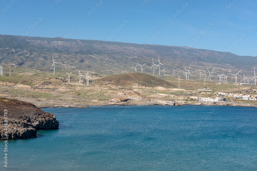Wind turbines lining the southern coast of the island, alternative source of energy with lower environmental footprint, as seen from the tiny village El Poris de Abona, Tenerife, Canary Islands, Spain