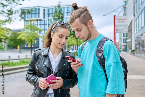 Teenage friends guy and girl standing together using smartphones