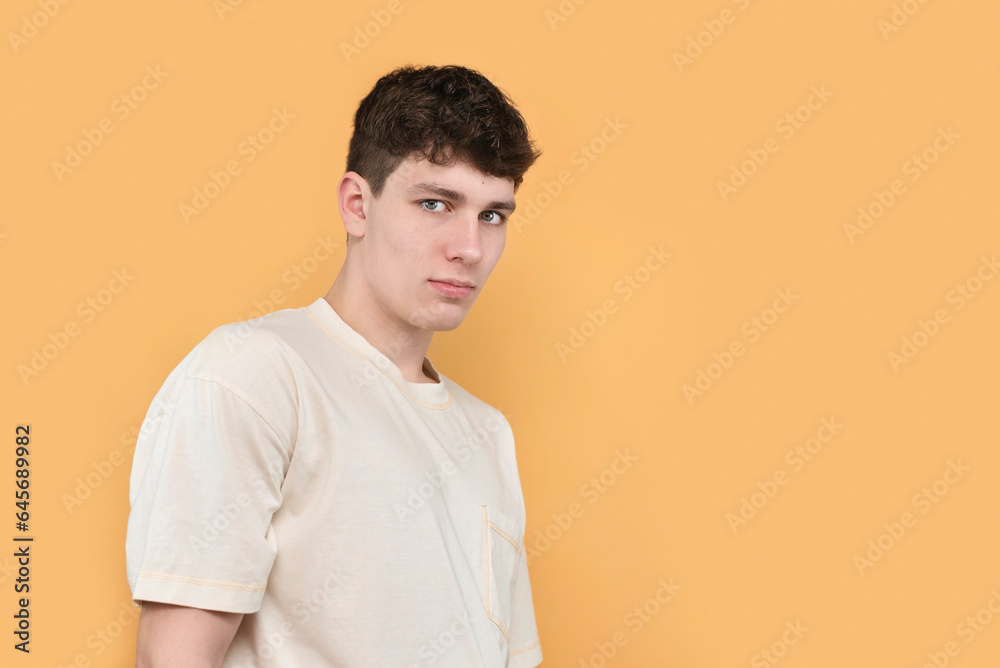 Young serious shy guy 18 years old on yellow background, copy space, advertisement. The boy has an inferiority complex, it is difficult for him to communicate with people Young serious shy guy 18 years old on yellow background, copy space, advertisement. The boy has an inferiority complex, it is difficult for him to communicate with people