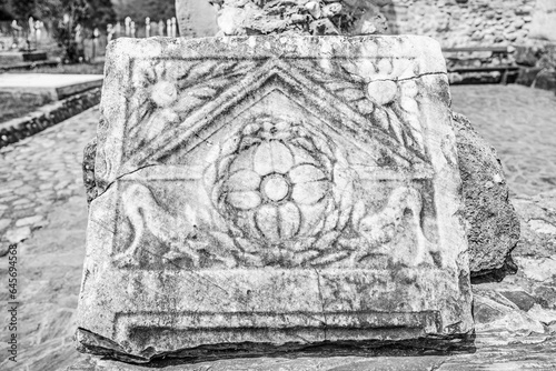 Ancient roman ruin at Densuș church yard, Hunedoara county, Transylvania, Romania; antique roman carved stone plaque in black and white photo