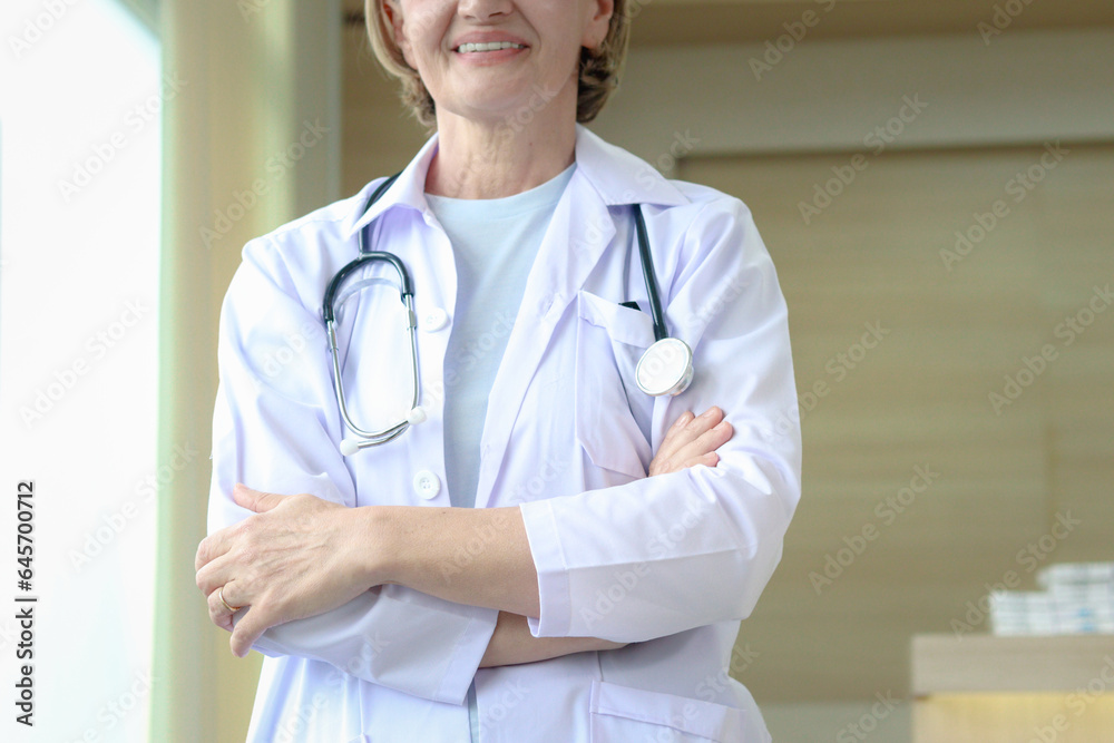 Smiling confident female doctor in white workwear with stethoscope, standing with arms crossed in clinic hospital. Professional senior woman doctor at medical workplace. Smiling confident female doctor in white workwear with stethoscope, standing with arms crossed in clinic hospital. Professional senior woman doctor at medical workplace.