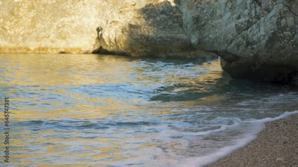Small sea waves at shore washing rock on sandy beach, closeup morning detail