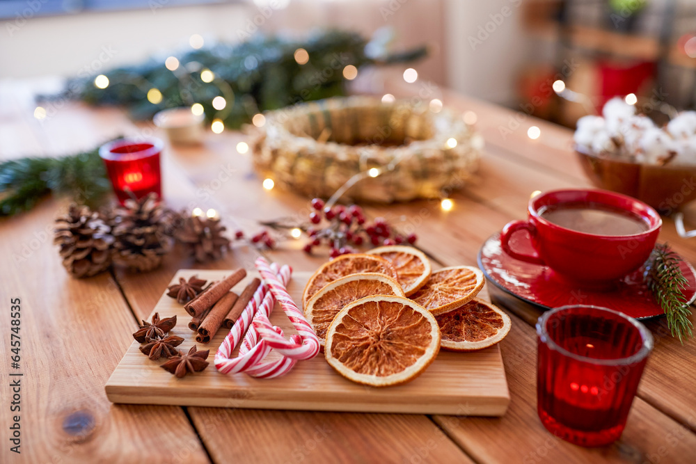 winter holidays, diy and hobby concept - close up of dry oranges, candy canes, christmas spices and decorations on wooden table