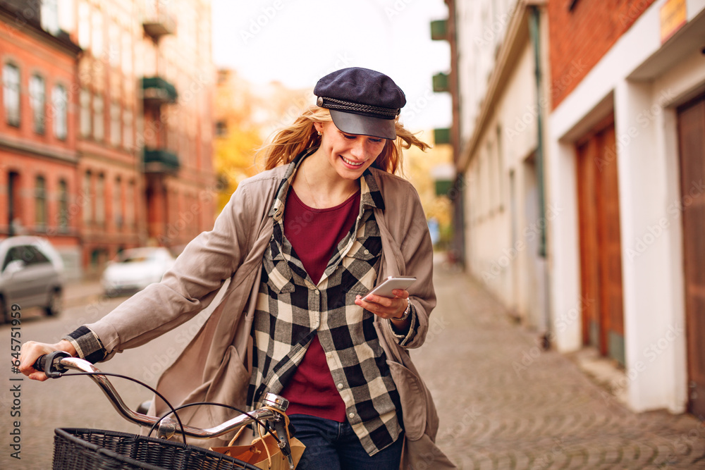 Young woman using a smartphone while pushing her bicycle in the city