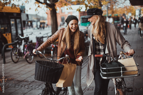 Young lesbian couple riding bicycles together while shopping in the city