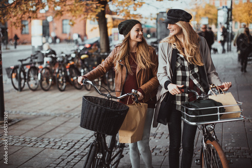 Young lesbian couple riding bicycles together while shopping in the city