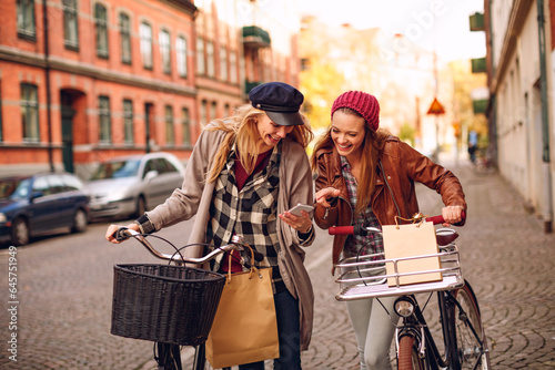 Young lesbian couple using a smartphone and riding bikes together while shopping in the city