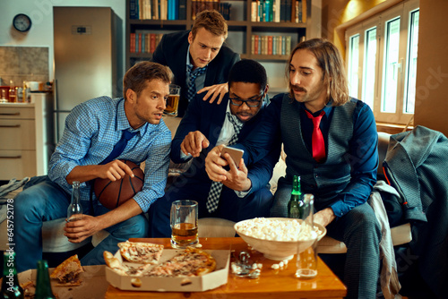 Young and diverse group of friends using a smartphone while watching a basketball game on the tv in the living room