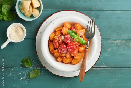 Potato gnocchi. Traditional homemade potato gnocchi with tomato sauce, basil and parmesan cheese on turquoise rustic kitchen table background. Traditional Italian food. Top view. photo