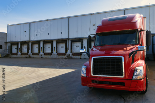 Red modern American semi truck parked at the docks, waiting to get loaded. Shipping and receiving, transportation business concept. Truck driving jobs.