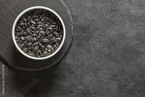 Sunflower seeds, unpeeled in white bowl, on slate stone plate round, dark background, top view