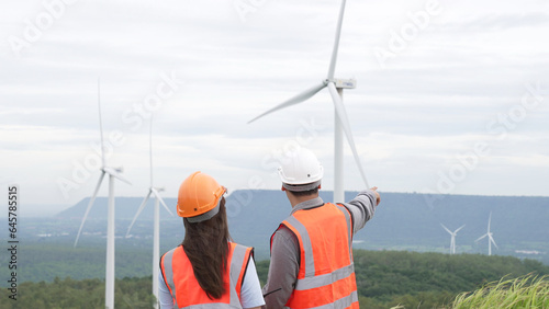 Male and female engineers working on a wind farm atop a hill or mountain in the rural. Progressive ideal for the future production of renewable, sustainable energy.