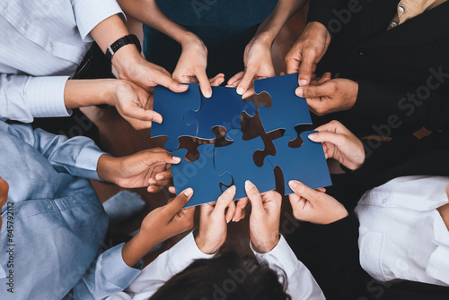 Diverse corporate officer workers collaborate in office, connecting puzzle pieces to represent partnership and teamwork. Unity and synergy in business concept by merging jigsaw puzzle. Concord