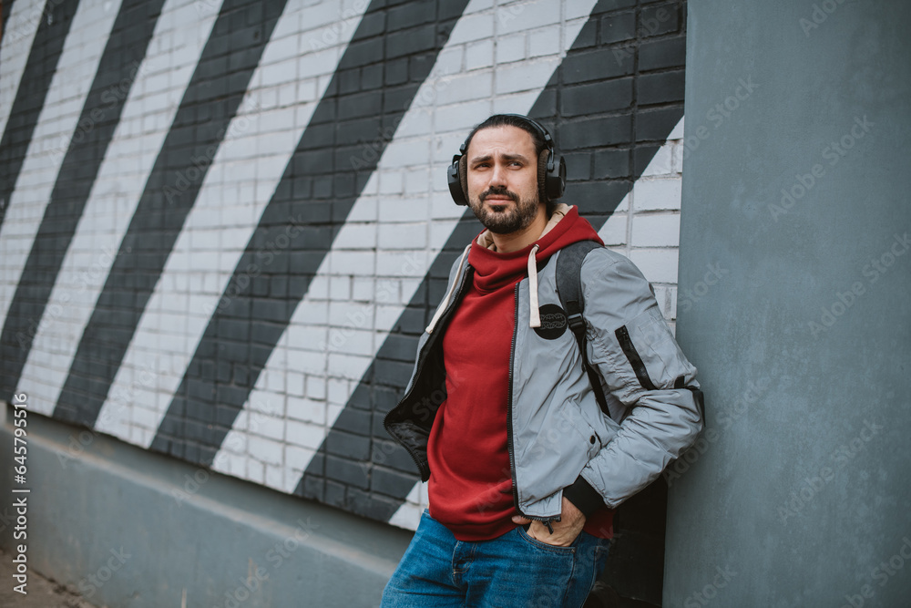 Portrait of a young man wearing headphones on a city background, against a wall with a geometric pattern. Portrait of a young man wearing headphones on a city background, against a wall with a geometric pattern.