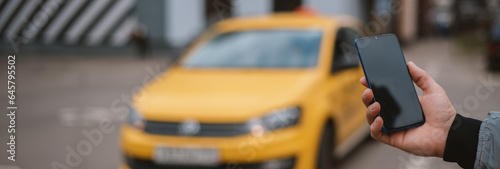 A man calls a taxi in the city through an app on his phone. Close-up. Yellow car on the background.