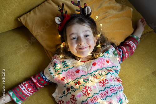 Happy cute girl in Christmas pullover playing with string light at home