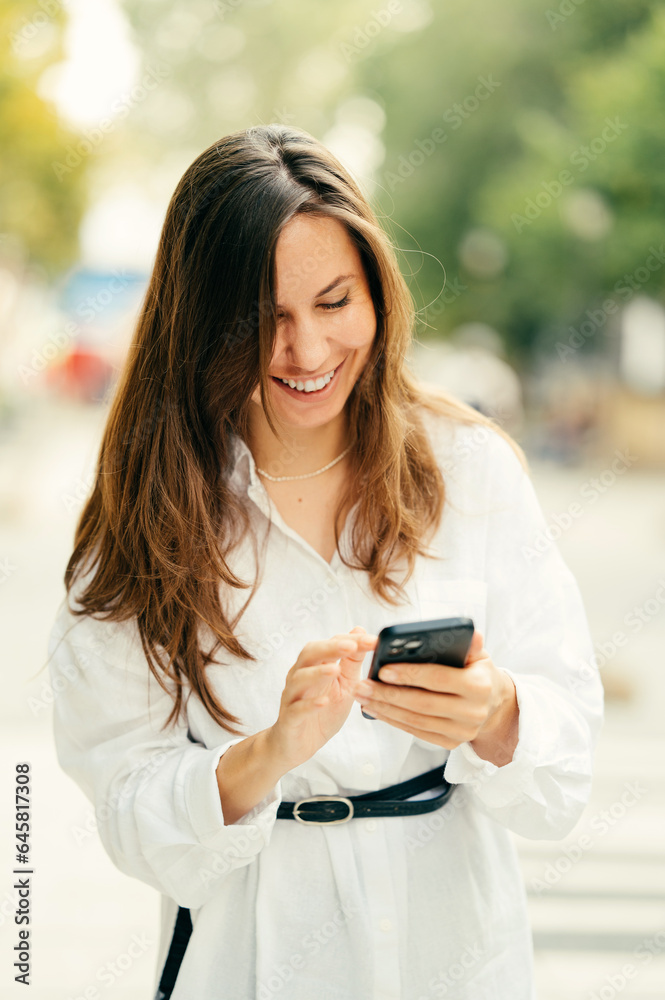 Ecstatic young woman in white enjoys summer while using her smart phone outdoors. Ecstatic young woman in white enjoys summer while using her smart phone outdoors.