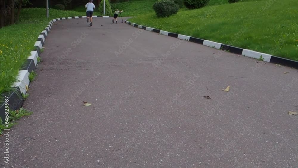 a boy in black shorts, colored sneakers and a girl in gray shorts and a blue T-shirt ride a blue scooter in the summer and do tricks on the asphalt. Children spend their free time outdoors.