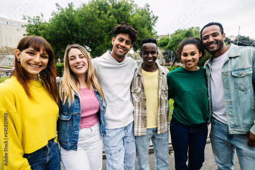 Young group of happy multiracial student friends looking at camera standing together outdoor. Smiling millennial people hugging each other posing for photo.