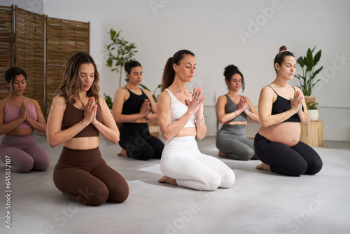Group of diverse fitness young women practicing yoga mudra exercises indoors. Concentrated meditating girls in class. Healthy lifestyle in community, female wellness and daily morning routines.  photo