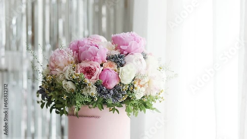 An elegant bouquet of fresh roses, peonies, and daisies in a pink box, beautifully arranged and placed by a light-filled window.