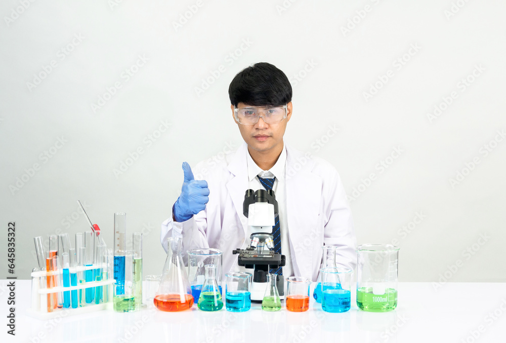 Portrait asian man student scientist Wearing a doctor gown in the lab looking hand at chemist. caused by mixing reagents in scientific research laboratories with test tubes and microscope on the table Portrait asian man student scientist Wearing a doctor gown in the lab looking hand at chemist. caused by mixing reagents in scientific research laboratories with test tubes and microscope on the table