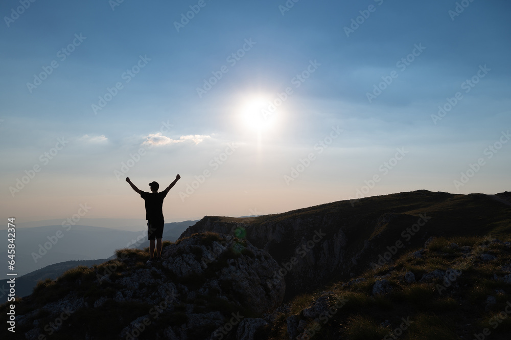 A happy man standing with hands up on the mountain top at sunrise concept od success victory