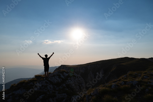 A happy man standing with hands up on the mountain top at sunrise concept od success victory