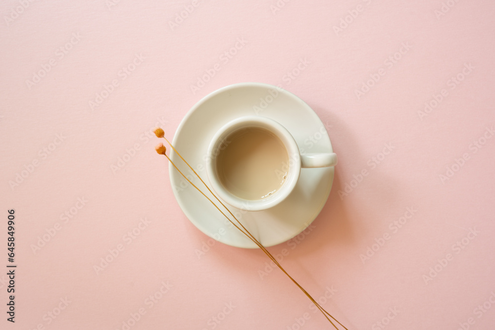 White cup of coffee with dry flower on pink background. top view