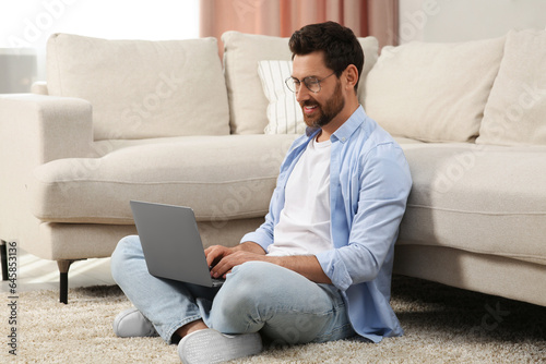 Man using laptop on floor near sofa at home