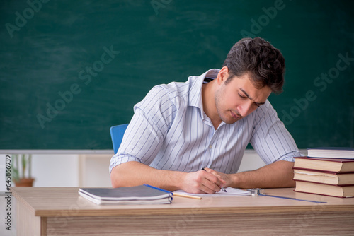 Young male teacher in front of green board