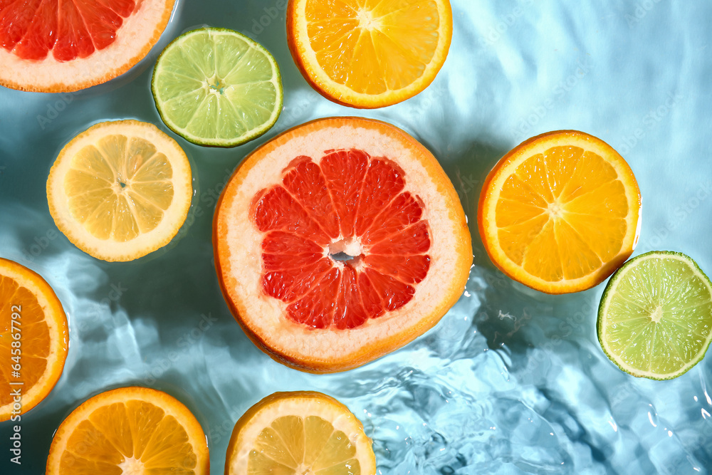 Different citrus fruit slices in water on blue background