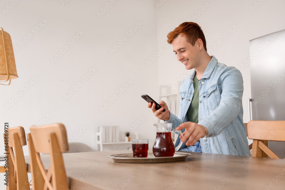 Young man with juice using mobile phone in kitchen Young man with juice using mobile phone in kitchen
