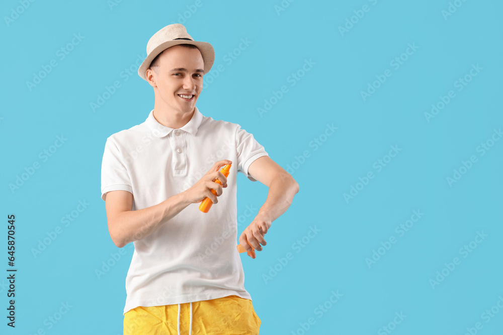 Young man applying sunscreen cream on blue background