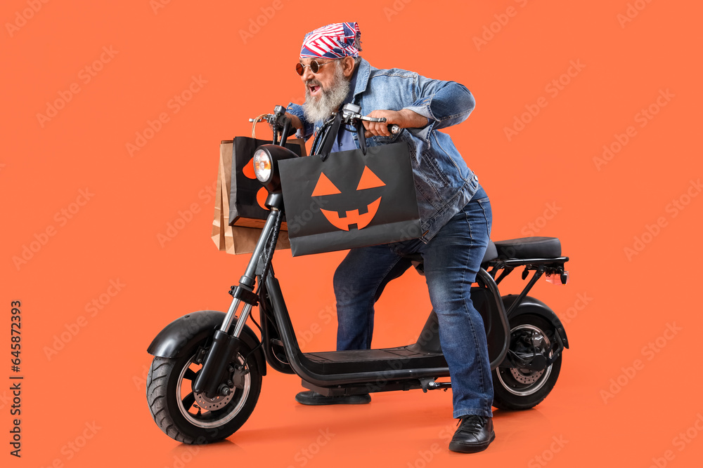 Mature biker with Halloween gift bags and scooter on color background Mature biker with Halloween gift bags and scooter on color background