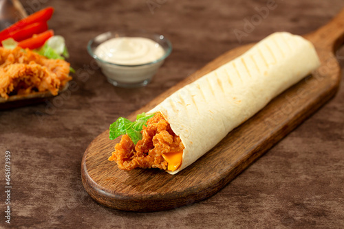 hand holding Tortilla wraps with crispy chicken breast, lettuce and vegetables, served with garlic cream sauce