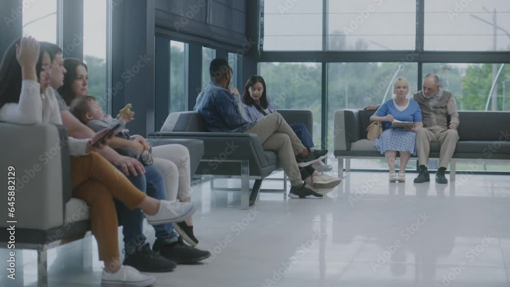 Diverse multiethnic people sit on couches in clinic lobby area, wait for appointment with doctor or medical test results. Waiting area in medical center with modern design. Healthcare system.