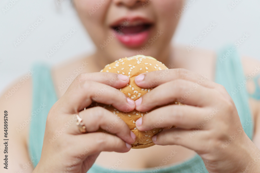 Happy oversize fat Asian women enjoy eating a pizza, hamburger, and French fry with drinking cola soda.