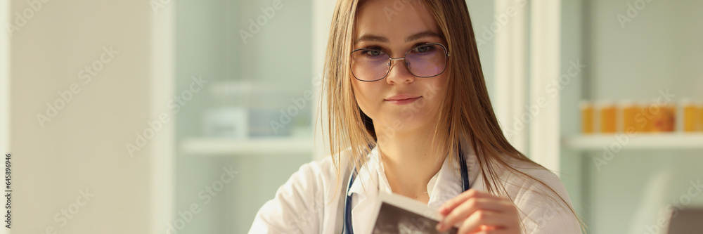 Young female doctor working with ultrasound scan results and looking at camera. Young female doctor working with ultrasound scan results and looking at camera.