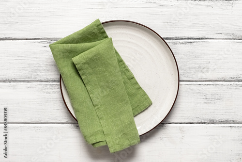 White plate with green napkin on a white wooden table. Top view, flat lay, copy space.