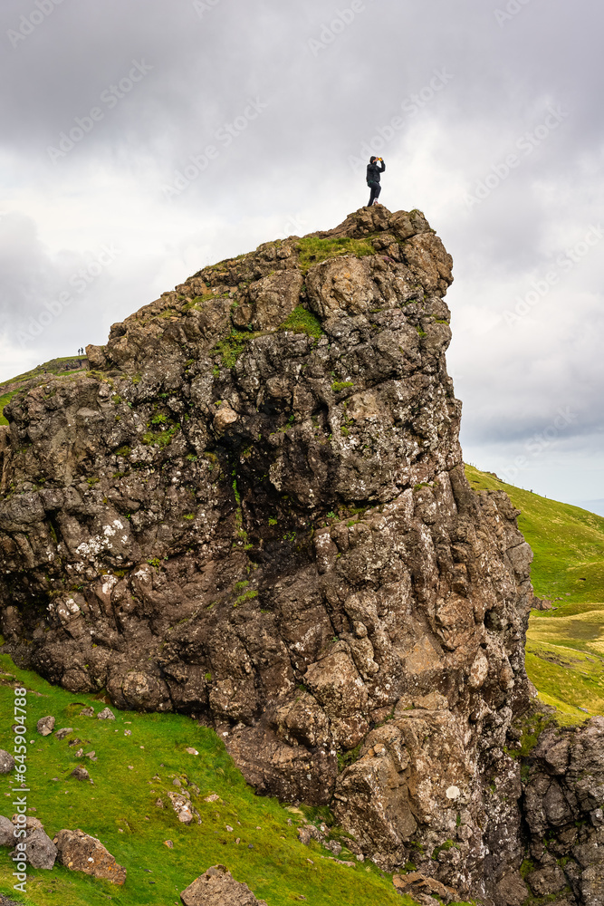 Hiker climbs on top of a rock formation taking a photo on the Isle of Skye, Scotland.
