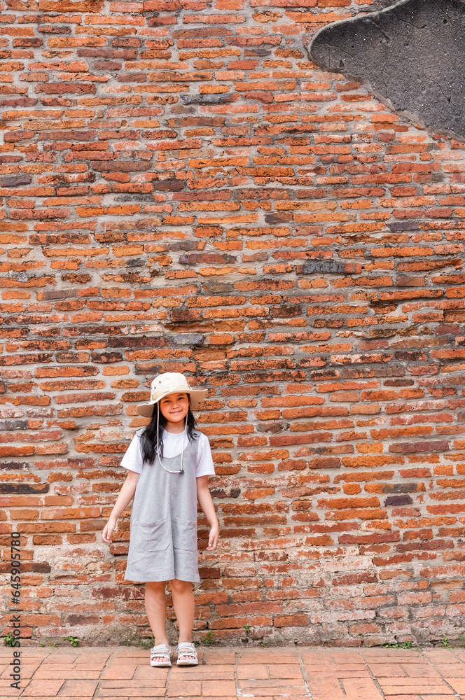 asian child smile or kid girl travel to retro portrait with brick wall background in ancient site and wat ratchaburana temple at ayutthaya old brickwork in Thailand for people tourist with copy space