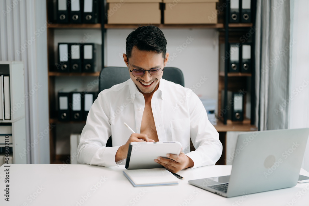 .Young handsome business man working at office with laptop, tablet and taking notes on the paper. .Young handsome business man working at office with laptop, tablet and taking notes on the paper.