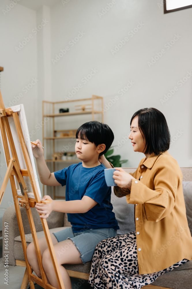 Asian Woman assisting young boy in painting on canvas. Happy woman looking at her painting .. Asian Woman assisting young boy in painting on canvas. Happy woman looking at her painting ..