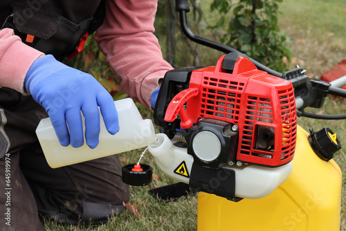 Foto A man in yellow gloves starts up a red trimmer to cut the lawn in autumn