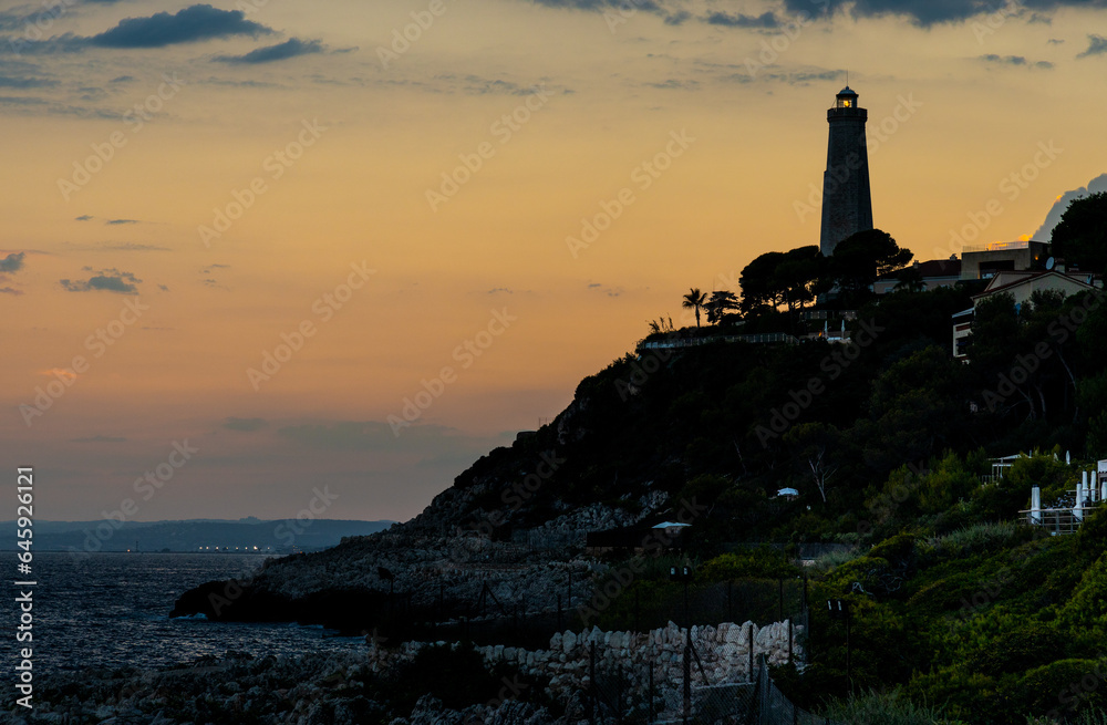 Sunset over rocky coast of Cap Ferrat cape with Phare Lighthouse near Saint-Jean-Cap-Ferrat resort town and Nice at French Riviera in France