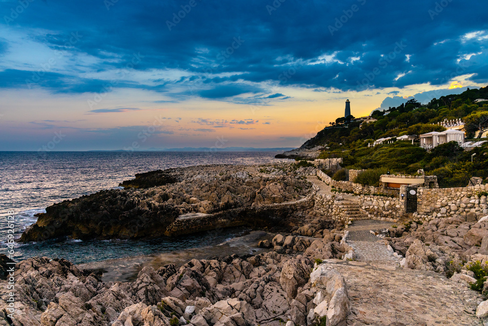 Fototapeta premium Sunset over rocky coast of Cap Ferrat cape with Phare Lighthouse near Saint-Jean-Cap-Ferrat resort town and Nice at French Riviera in France