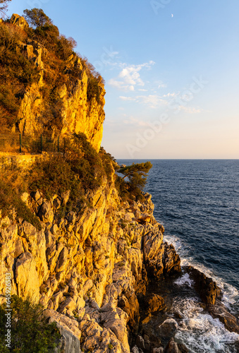 Rocks and cliffs shoreline sunset landscape of Cap Ferrat cape hosting Saint-Jean-Cap-Ferrat resort town on at French Riviera of Mediterranean Sea near Nice in France